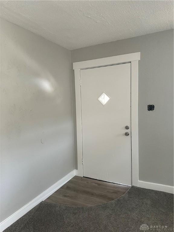 doorway to outside featuring a textured ceiling, baseboards, and dark colored carpet