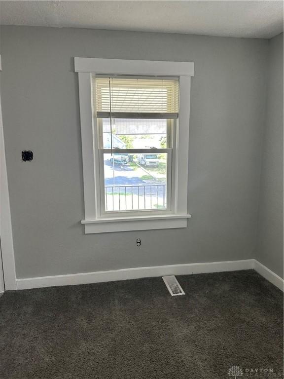 spare room with dark colored carpet, visible vents, and baseboards