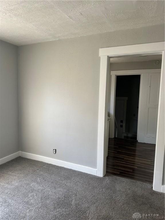 empty room with carpet flooring, a textured ceiling, and baseboards