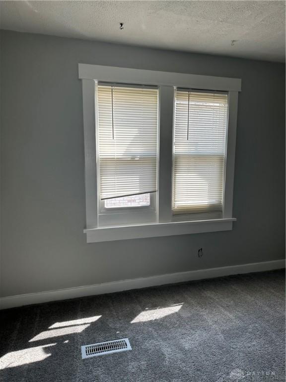 empty room featuring visible vents, carpet flooring, a textured ceiling, and plenty of natural light