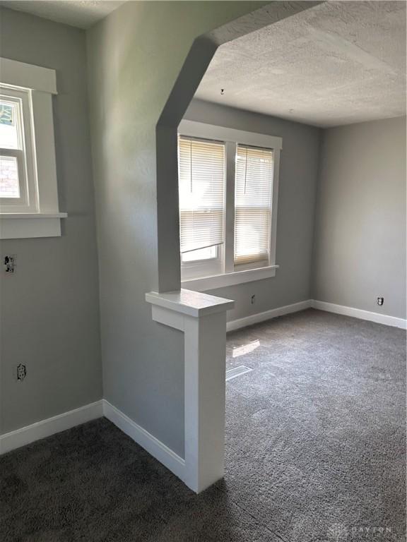 carpeted spare room featuring a textured ceiling and baseboards