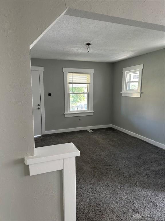 empty room with dark colored carpet, baseboards, a textured ceiling, and a wealth of natural light