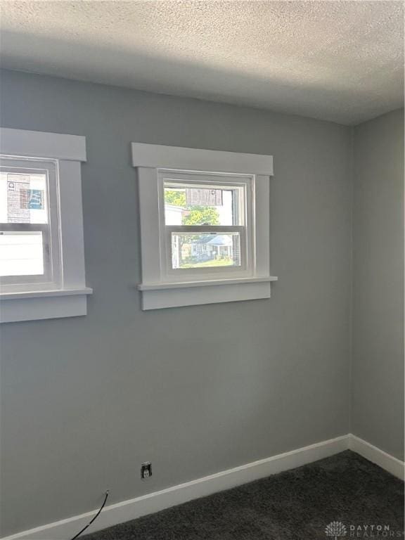 empty room featuring dark colored carpet, baseboards, and a textured ceiling