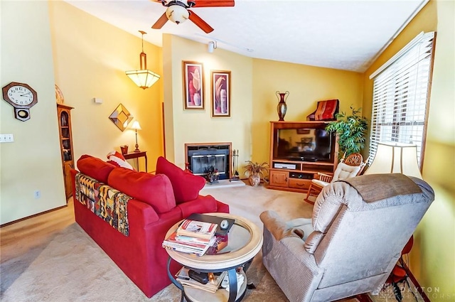 living area with carpet floors, a glass covered fireplace, a ceiling fan, and vaulted ceiling