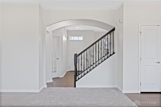 foyer entrance featuring baseboards, arched walkways, and stairway