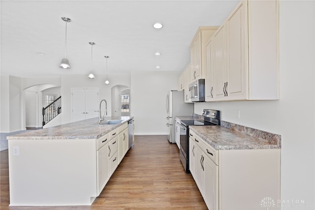 kitchen with a sink, arched walkways, light wood-style floors, and appliances with stainless steel finishes