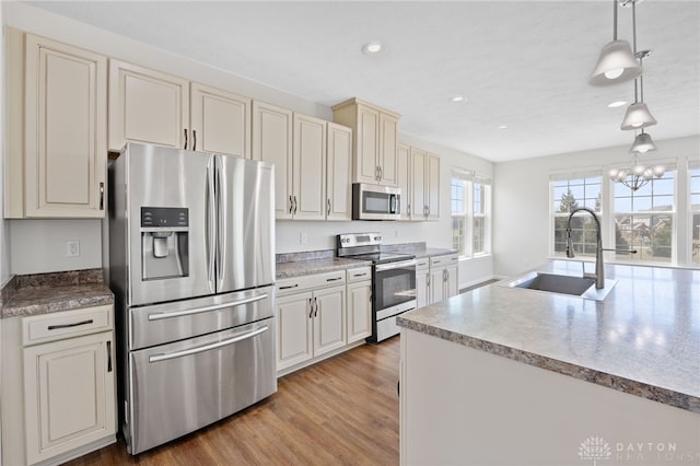 kitchen with pendant lighting, a sink, wood finished floors, stainless steel appliances, and an inviting chandelier