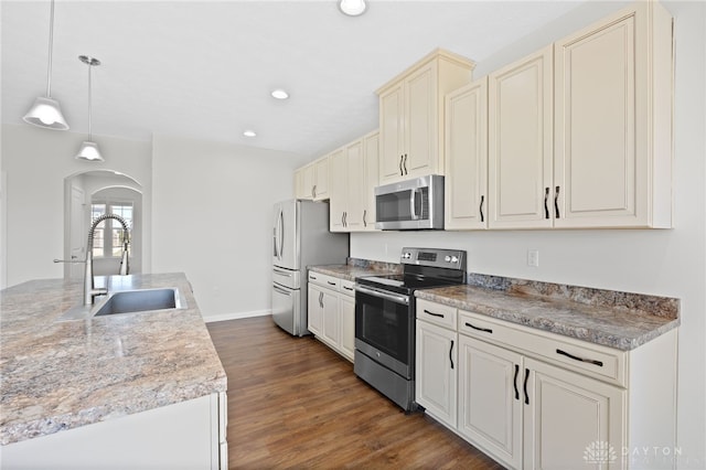 kitchen featuring dark wood-style floors, appliances with stainless steel finishes, cream cabinets, arched walkways, and a sink