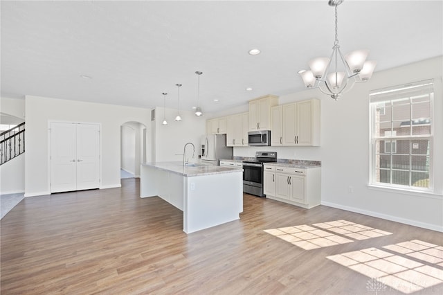 kitchen with light wood finished floors, an inviting chandelier, arched walkways, a sink, and appliances with stainless steel finishes