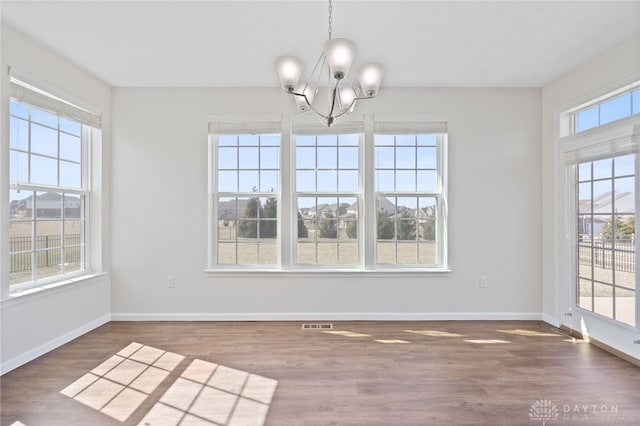 unfurnished dining area with an inviting chandelier, wood finished floors, baseboards, and visible vents