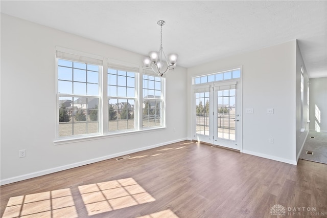 unfurnished dining area with a notable chandelier, baseboards, visible vents, and wood finished floors