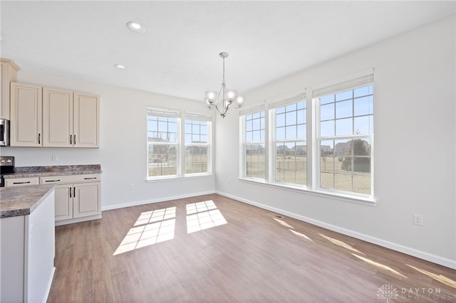 unfurnished dining area with recessed lighting, baseboards, an inviting chandelier, and light wood-style flooring