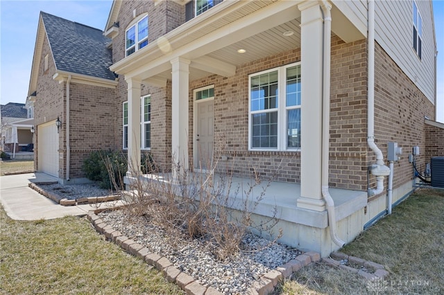 view of exterior entry featuring brick siding, covered porch, driveway, and a garage