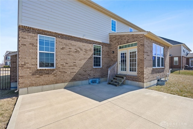 rear view of house with entry steps, a patio area, fence, and brick siding