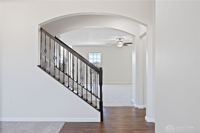 staircase featuring arched walkways, baseboards, a ceiling fan, and wood finished floors