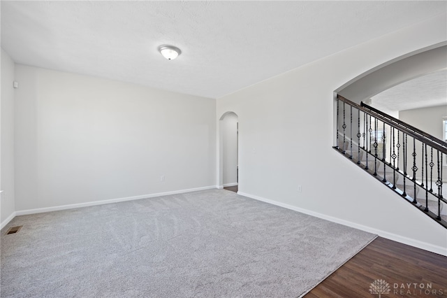 unfurnished room featuring visible vents, dark wood finished floors, stairway, arched walkways, and baseboards