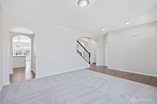 unfurnished living room with arched walkways, stairway, dark carpet, and a notable chandelier