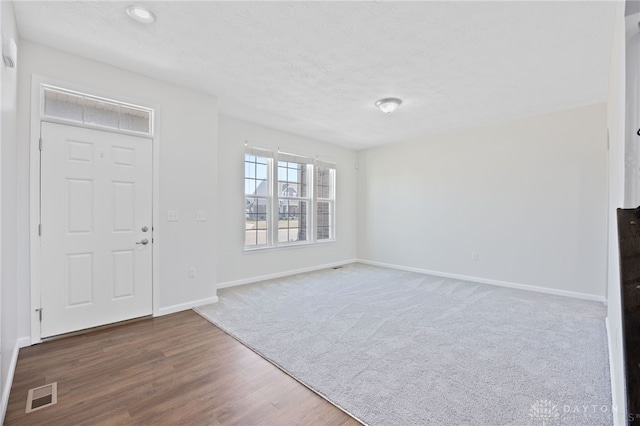 foyer with visible vents, a textured ceiling, baseboards, and wood finished floors