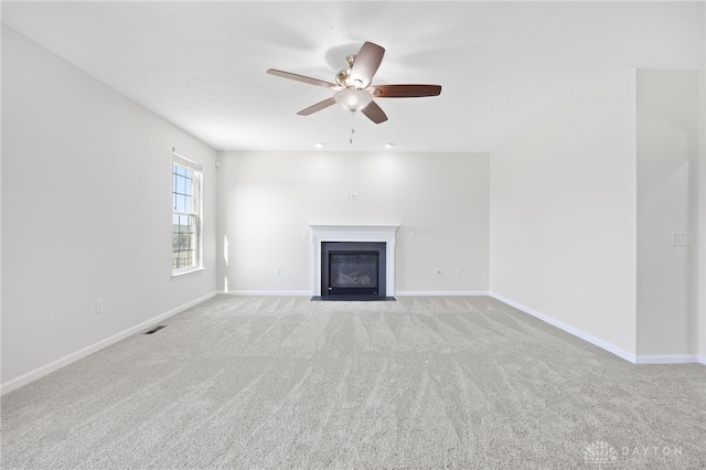 unfurnished living room featuring light colored carpet, a fireplace with flush hearth, a ceiling fan, and visible vents