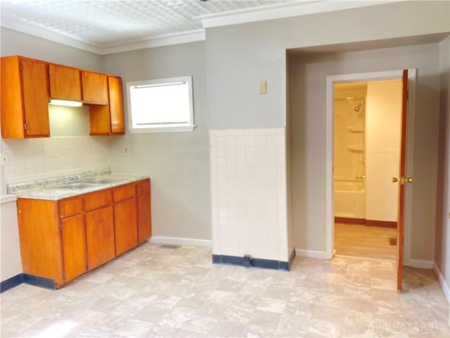 kitchen with a sink, baseboards, brown cabinetry, and light countertops