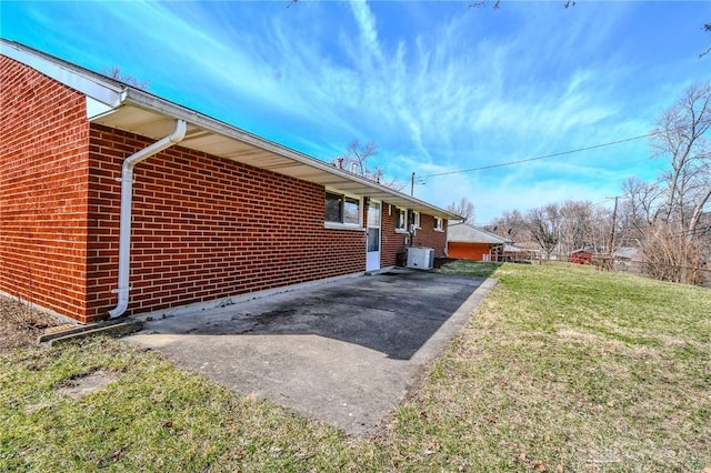 view of property exterior featuring driveway, a yard, brick siding, and central AC