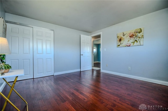 unfurnished bedroom with dark wood-style floors, baseboards, and a closet