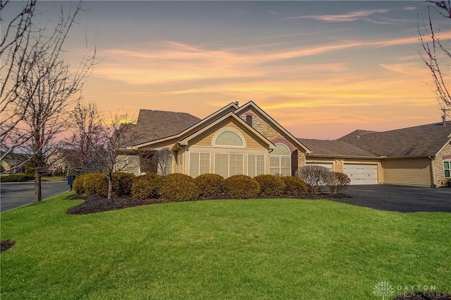 ranch-style home with aphalt driveway, a lawn, and a garage