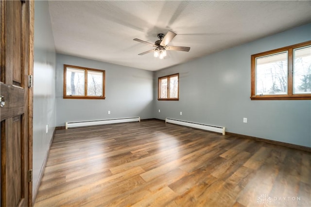 empty room featuring baseboard heating, wood finished floors, and a ceiling fan