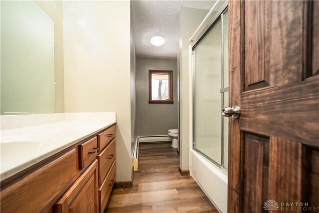 bathroom with vanity, wood finished floors, a textured ceiling, toilet, and baseboard heating
