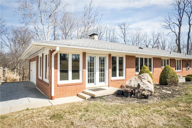 back of property with french doors, brick siding, a garage, and a chimney