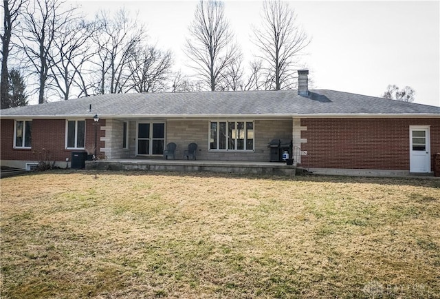 rear view of house featuring brick siding, a lawn, a chimney, and a patio