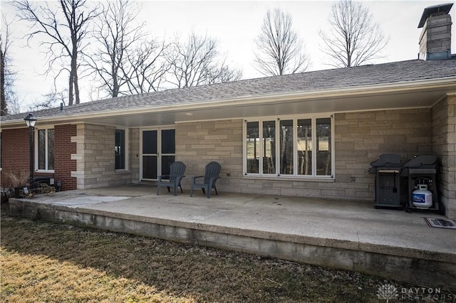 back of house featuring stone siding, a patio, a chimney, and a shingled roof