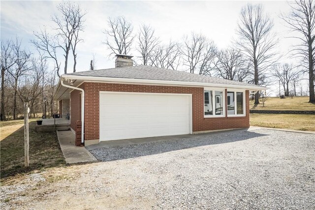 view of side of property with driveway, a yard, an attached garage, a chimney, and brick siding