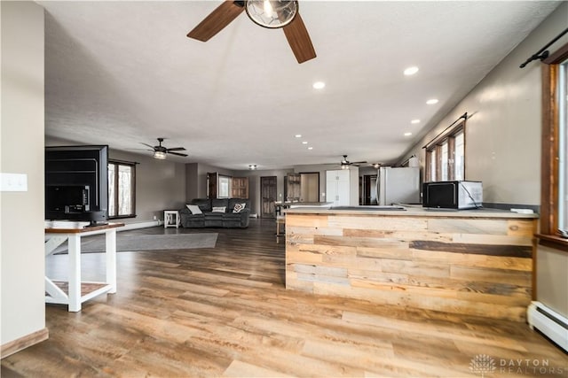 kitchen featuring a baseboard heating unit, wood finished floors, a ceiling fan, and a peninsula