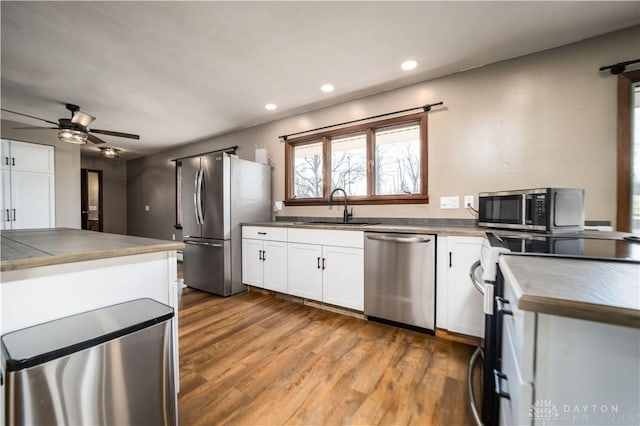 kitchen with a ceiling fan, wood finished floors, a sink, stainless steel appliances, and white cabinetry