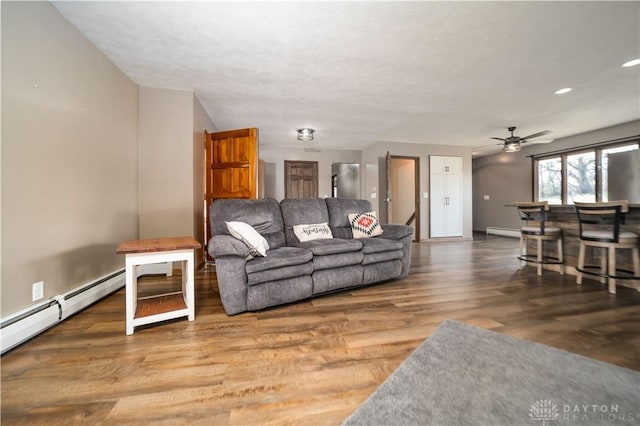 living room featuring wood finished floors, baseboards, a ceiling fan, a baseboard heating unit, and a dry bar