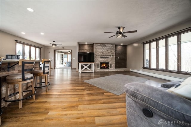 living area with a baseboard radiator, wood finished floors, ceiling fan, and a fireplace