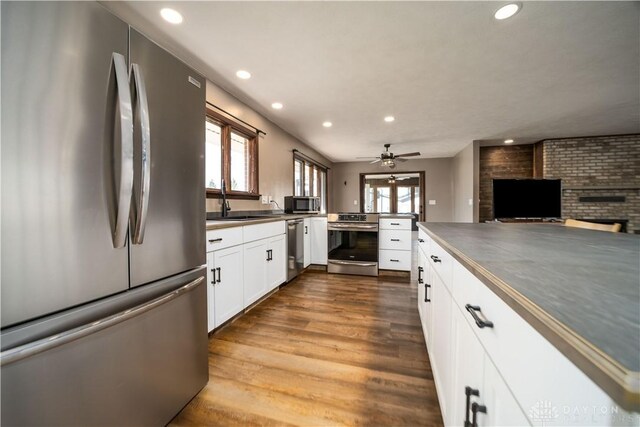 kitchen featuring dark countertops, appliances with stainless steel finishes, dark wood-style floors, white cabinetry, and a sink