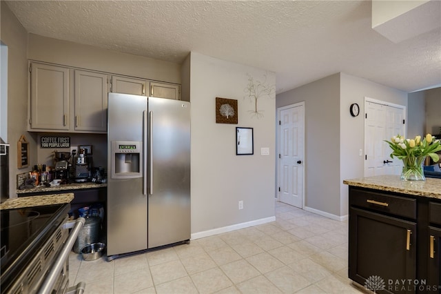 kitchen with light tile patterned floors, light stone countertops, baseboards, a textured ceiling, and stainless steel fridge