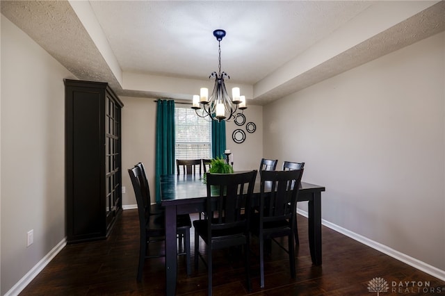 dining room with a tray ceiling, a textured ceiling, dark wood-style floors, an inviting chandelier, and baseboards