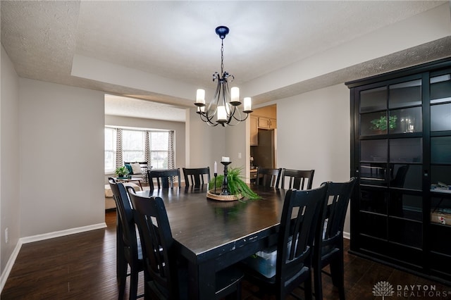 dining area featuring dark wood-style floors, a notable chandelier, a textured ceiling, and baseboards