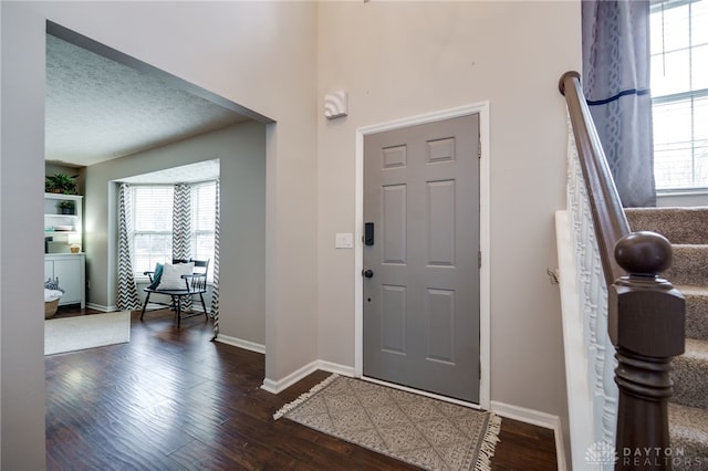 foyer entrance featuring dark wood finished floors, baseboards, and a textured ceiling