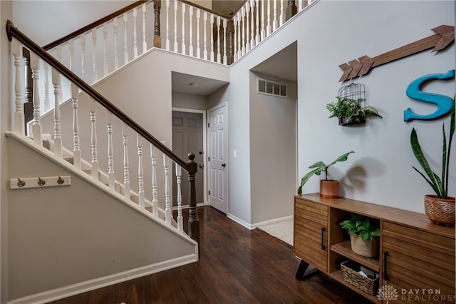 entrance foyer with visible vents, baseboards, stairway, a towering ceiling, and wood finished floors