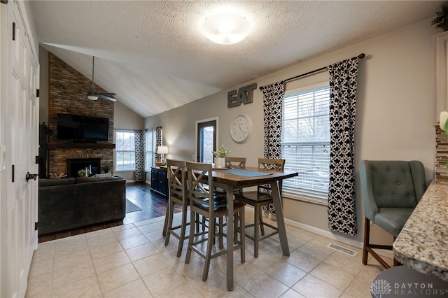 dining room featuring light tile patterned floors, a brick fireplace, a textured ceiling, and lofted ceiling