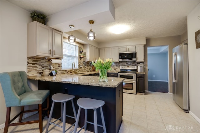 kitchen featuring light stone counters, a peninsula, light tile patterned flooring, stainless steel appliances, and a sink