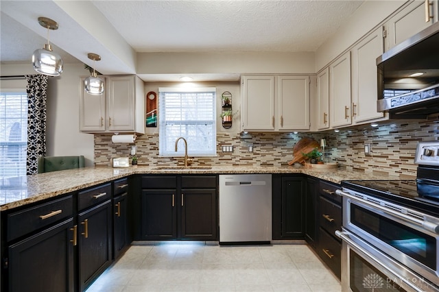 kitchen with backsplash, light stone counters, a wealth of natural light, appliances with stainless steel finishes, and a sink