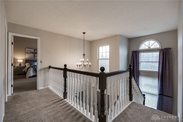 hallway featuring a chandelier, carpet flooring, a healthy amount of sunlight, and an upstairs landing