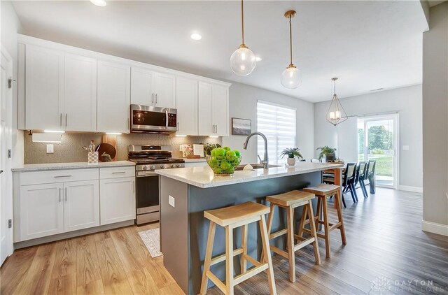 1002 Belfast Dr, Sugarcreek Township, OH 45440 - kitchen with a breakfast bar, an island with sink, tasteful backsplash, stainless steel appliances, and light wood-style floors