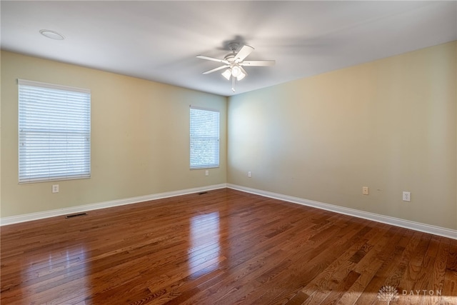 spare room featuring dark wood-type flooring, a ceiling fan, visible vents, and baseboards