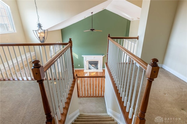 stairs with carpet flooring, ceiling fan with notable chandelier, baseboards, and high vaulted ceiling
